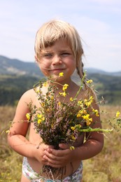 Photo of Smiling little girl with bouquet of wildflowers at field