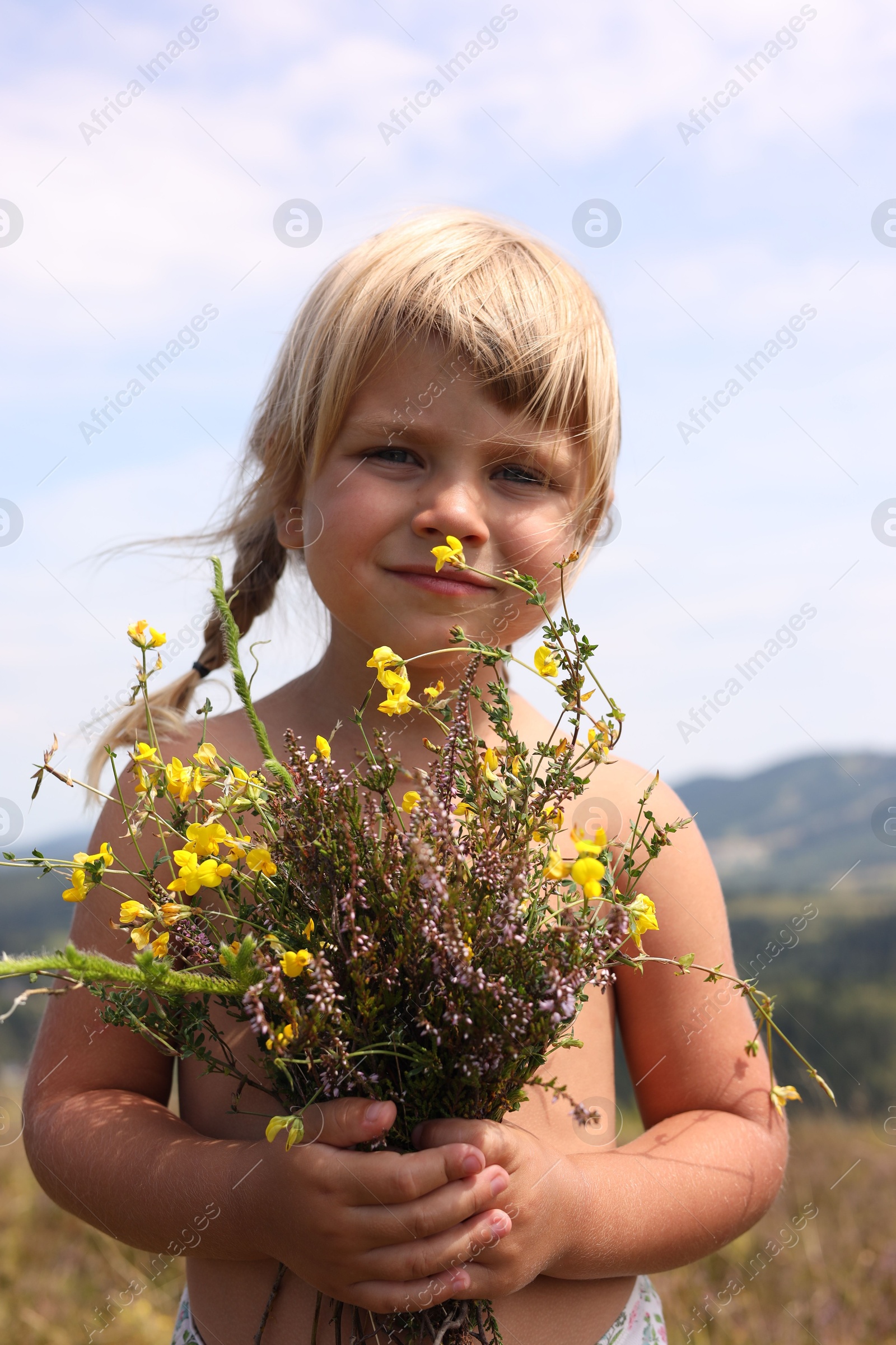 Photo of Smiling little girl with bouquet of wildflowers at field