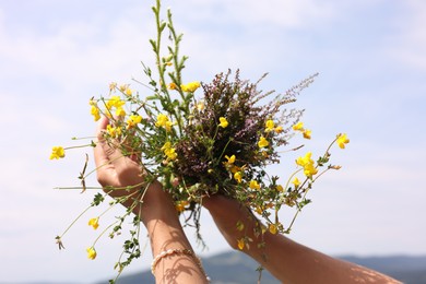 Woman holding bouquet of wild yellow flowers outdoors, closeup