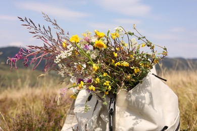 Photo of Bouquet of beautiful yellow flowers and backpack near mountains outdoors, closeup