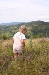 Photo of Cute little girl standing on meadow near mountains, back view