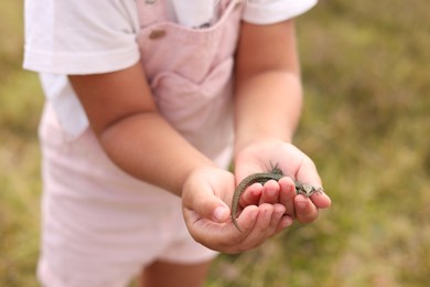 Photo of Little girl holding small lizard outdoors, closeup