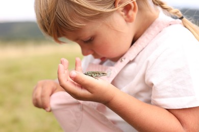 Photo of Happy little girl holding small lizard outdoors