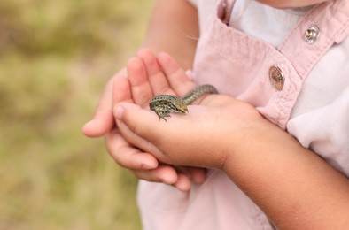 Photo of Little girl holding small lizard outdoors, closeup