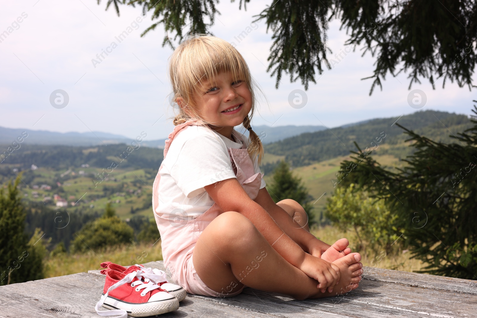 Photo of Cute little girl with shoes sitting on wooden deck outdoors