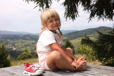 Photo of Cute little girl with shoes sitting on wooden deck outdoors