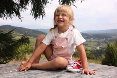 Cute little girl with shoes sitting on wooden deck outdoors