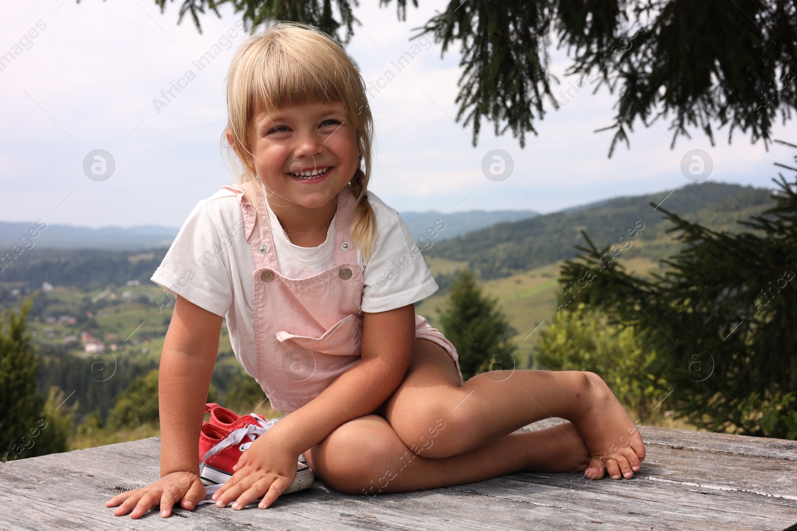 Photo of Cute little girl with shoes sitting on wooden deck outdoors