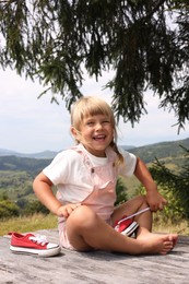 Cute little girl with shoes sitting on wooden deck outdoors