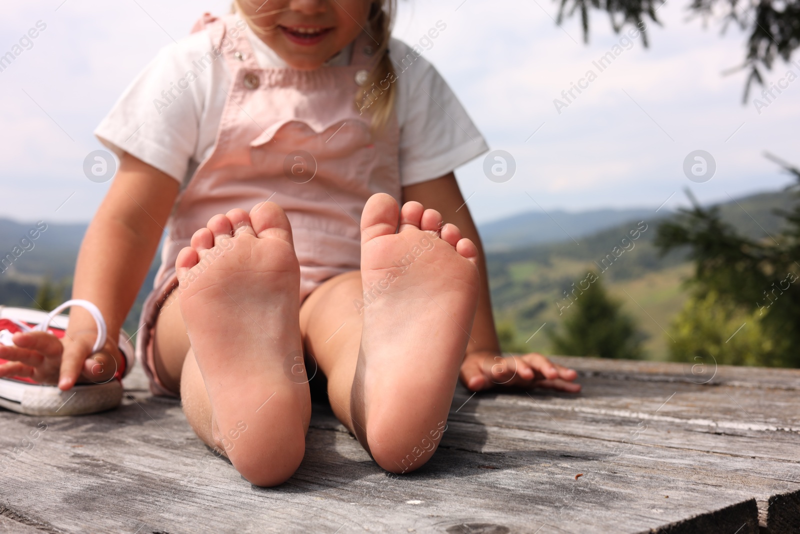 Photo of Little girl sitting on wooden deck outdoors, closeup