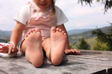 Little girl sitting on wooden deck outdoors, closeup