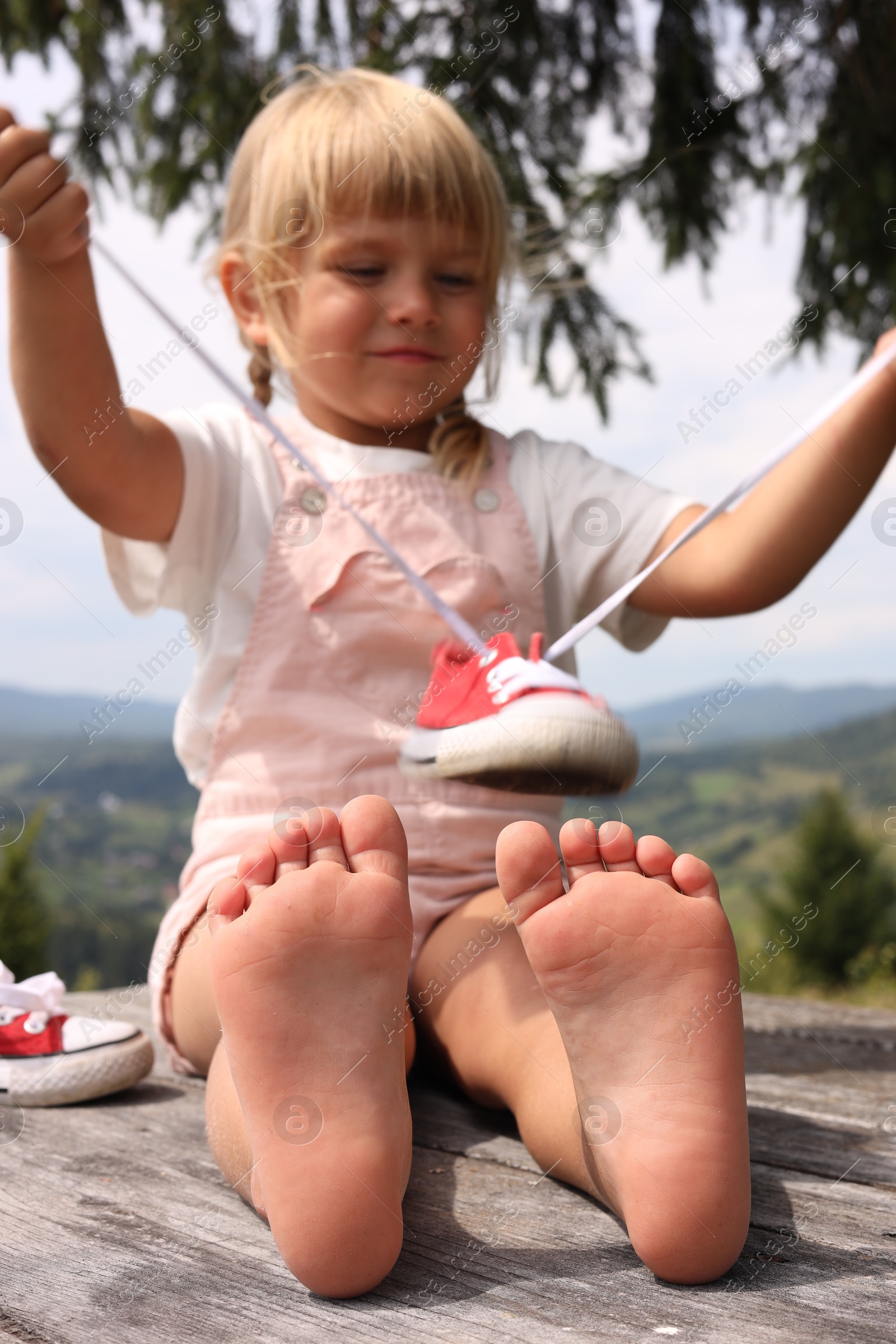 Photo of Cute little girl sitting on wooden deck outdoors, selective focus