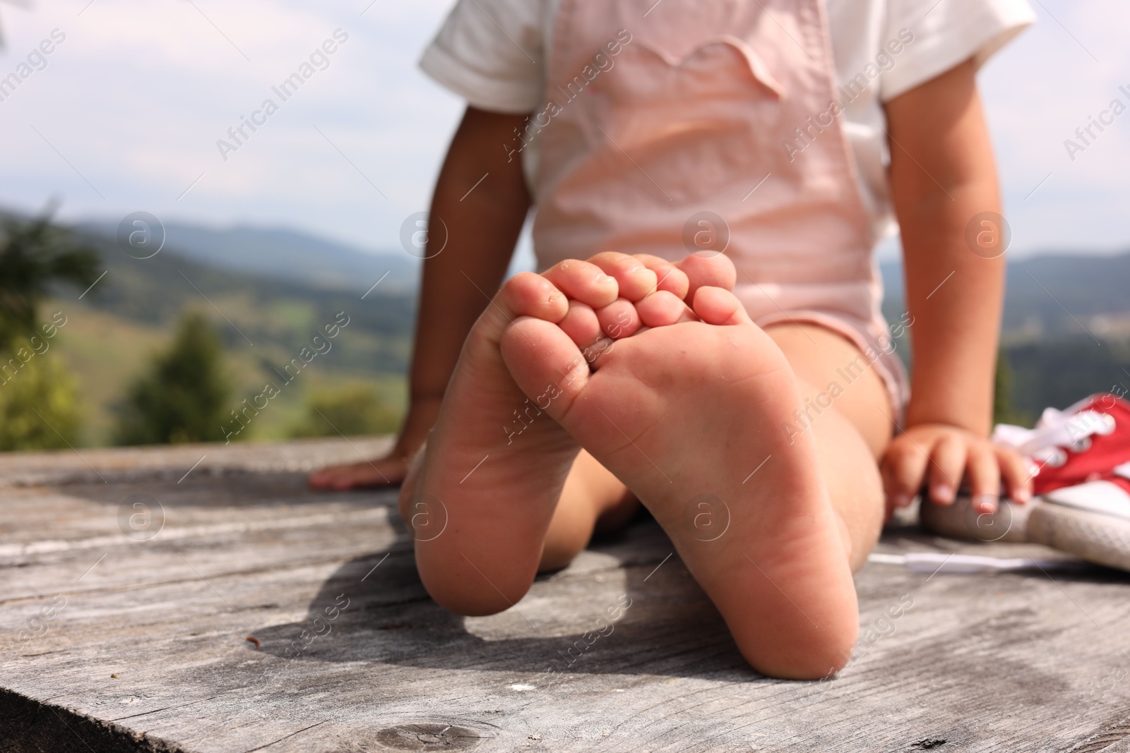 Photo of Little girl sitting on wooden deck outdoors, closeup