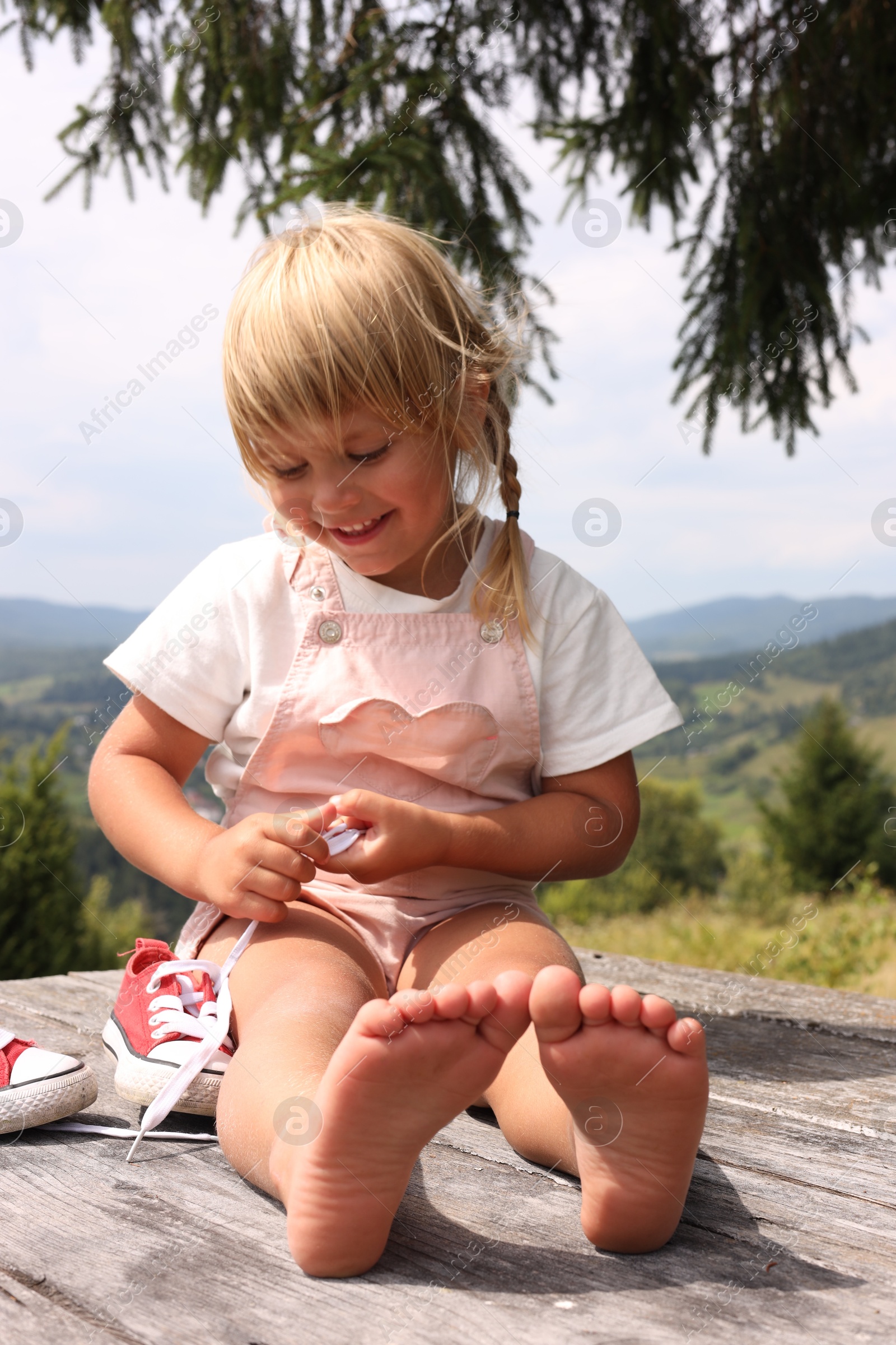 Photo of Cute little girl sitting on wooden deck in mountains