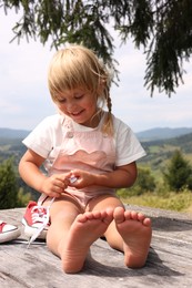 Photo of Cute little girl sitting on wooden deck in mountains