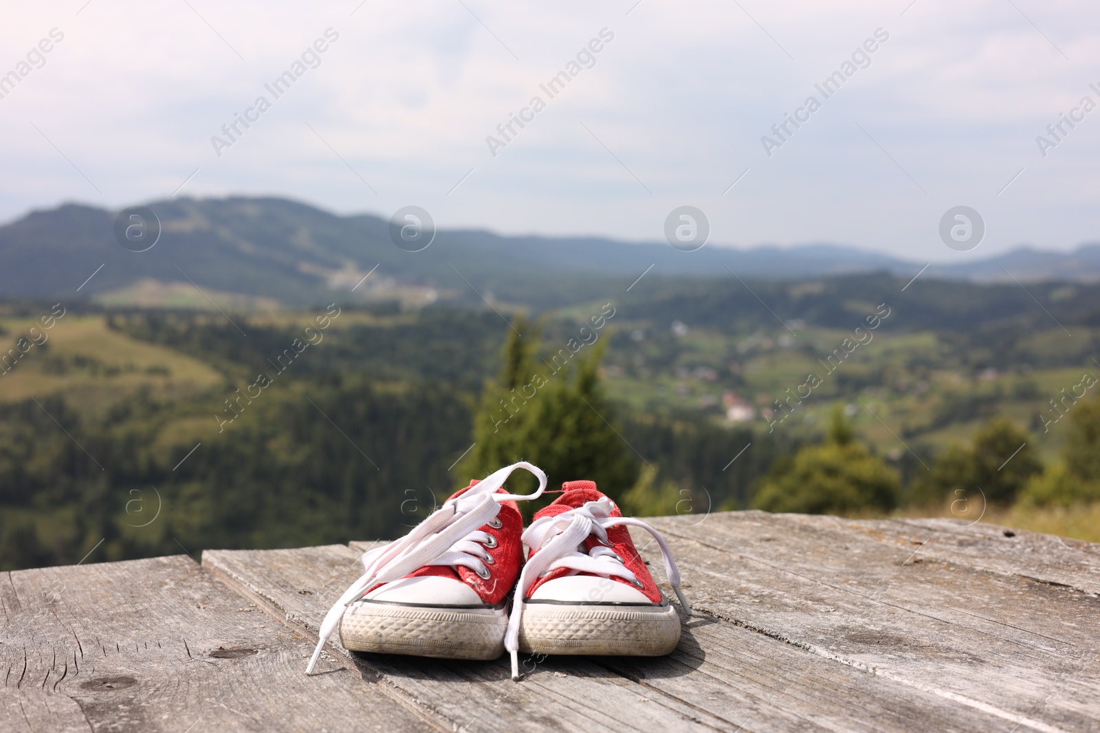 Photo of Pair of red shoes on wooden surface in mountains, space for text