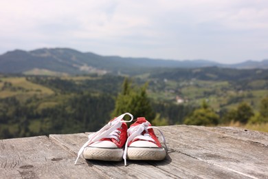 Pair of red shoes on wooden surface in mountains, space for text