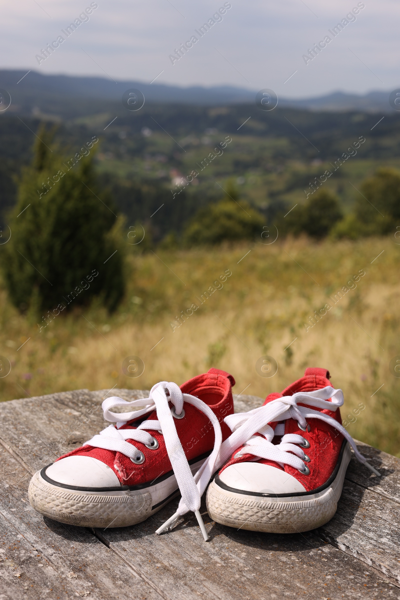 Photo of Pair of red shoes on wooden surface in mountains, space for text