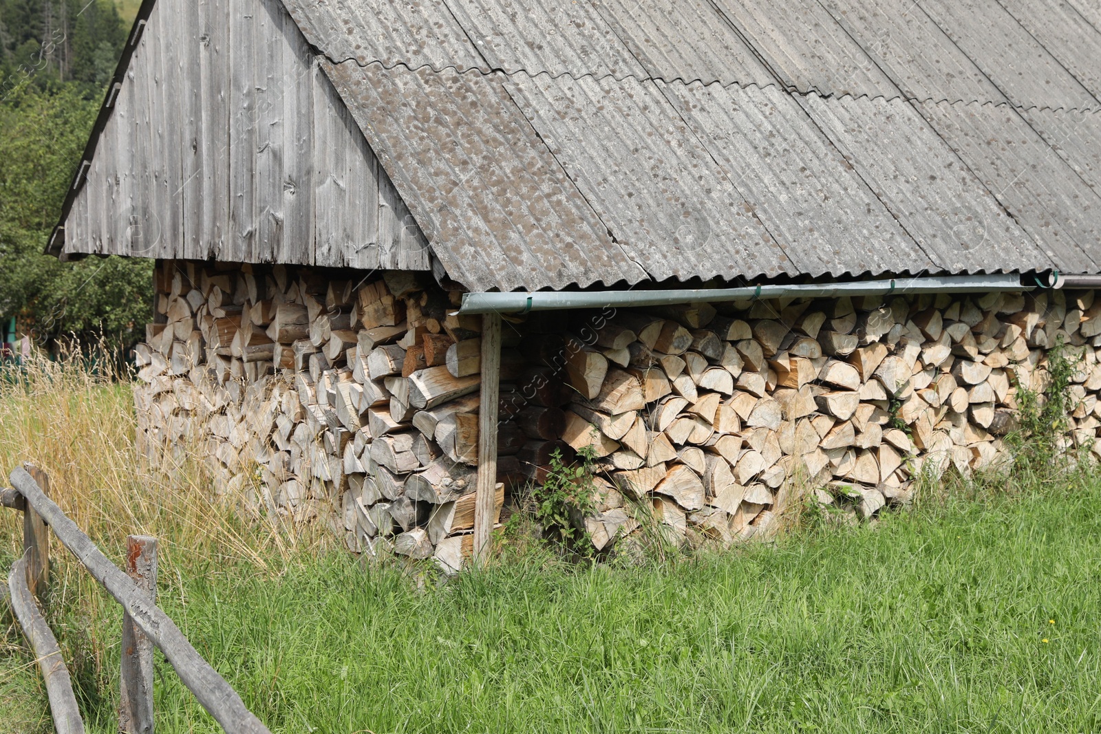 Photo of Stacked cut firewood in outdoor warehouse on sunny day