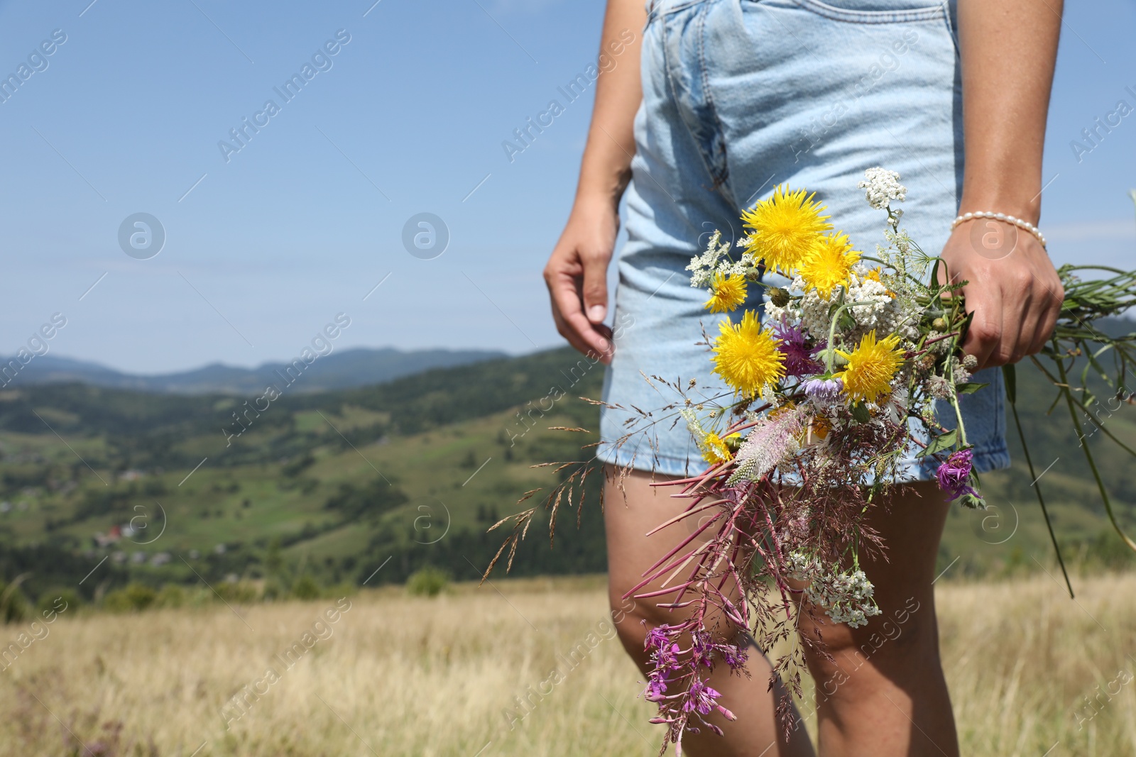 Photo of Woman holding bouquet of wild flowers outdoors, closeup