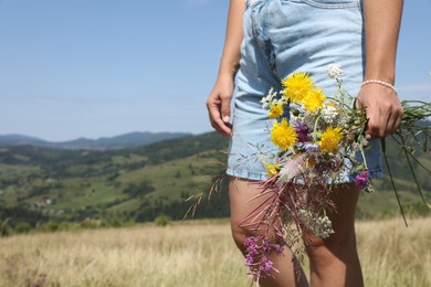 Photo of Woman holding bouquet of wild flowers outdoors, closeup