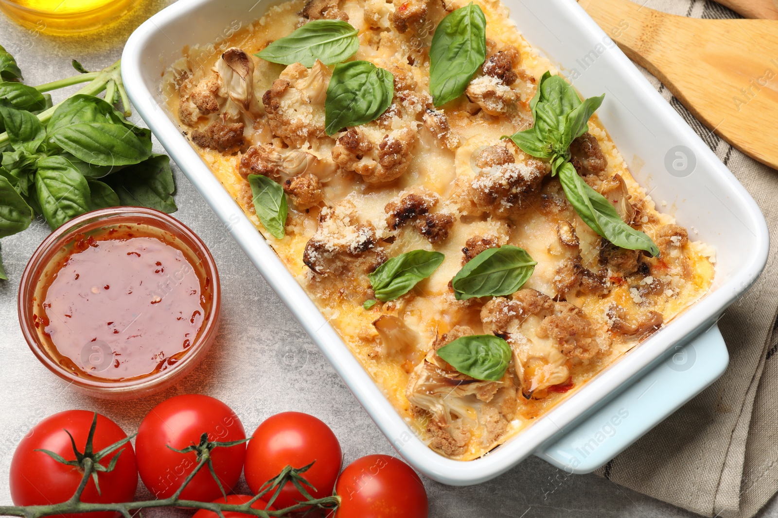 Photo of Tasty baked cauliflower in baking dish, basil, sauce and tomatoes on light grey table, top view