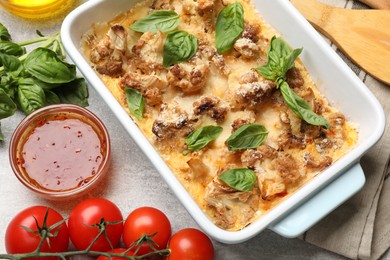 Photo of Tasty baked cauliflower in baking dish, basil, sauce and tomatoes on light grey table, top view