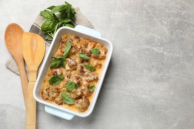 Photo of Tasty baked cauliflower in baking dish and basil on light grey table, top view. Space for text