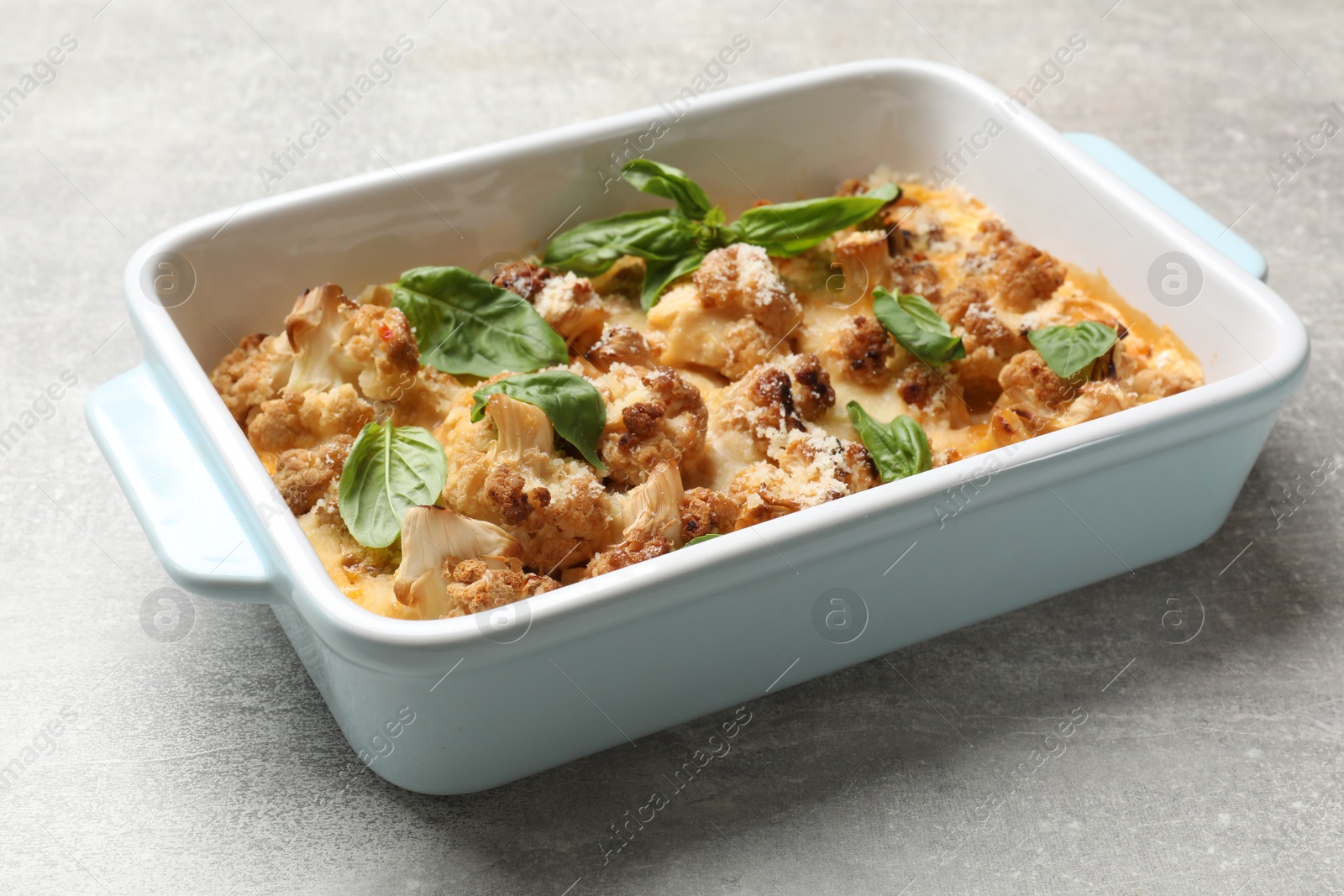 Photo of Tasty baked cauliflower and basil in baking dish on light grey table, closeup