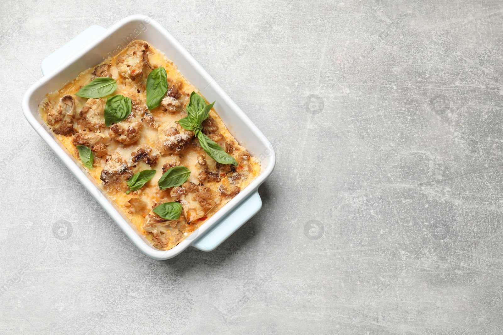 Photo of Tasty baked cauliflower and basil in baking dish on light grey table, top view. Space for text