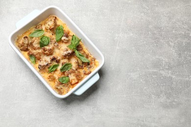 Photo of Tasty baked cauliflower and basil in baking dish on light grey table, top view. Space for text