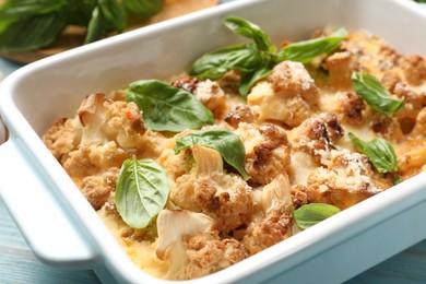 Photo of Tasty baked cauliflower and basil in baking dish on table, closeup