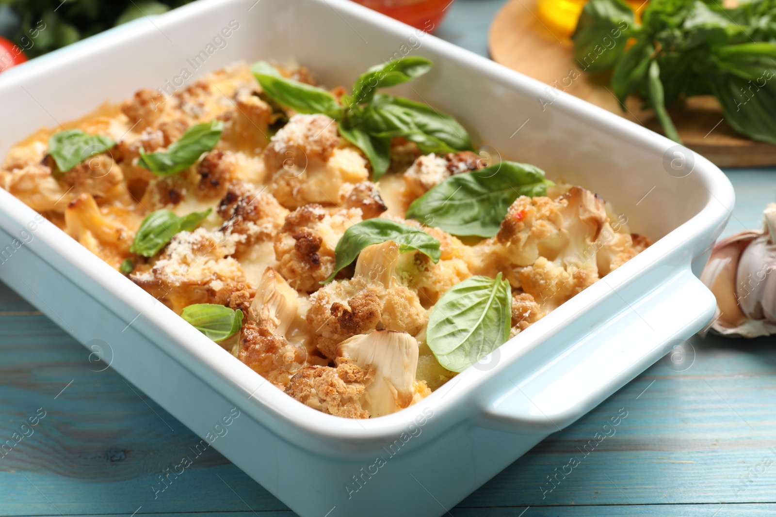 Photo of Tasty baked cauliflower and basil in baking dish on light blue wooden table, closeup