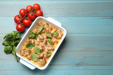 Photo of Tasty baked cauliflower in baking dish, basil and tomatoes on light blue wooden table, top view. Space for text