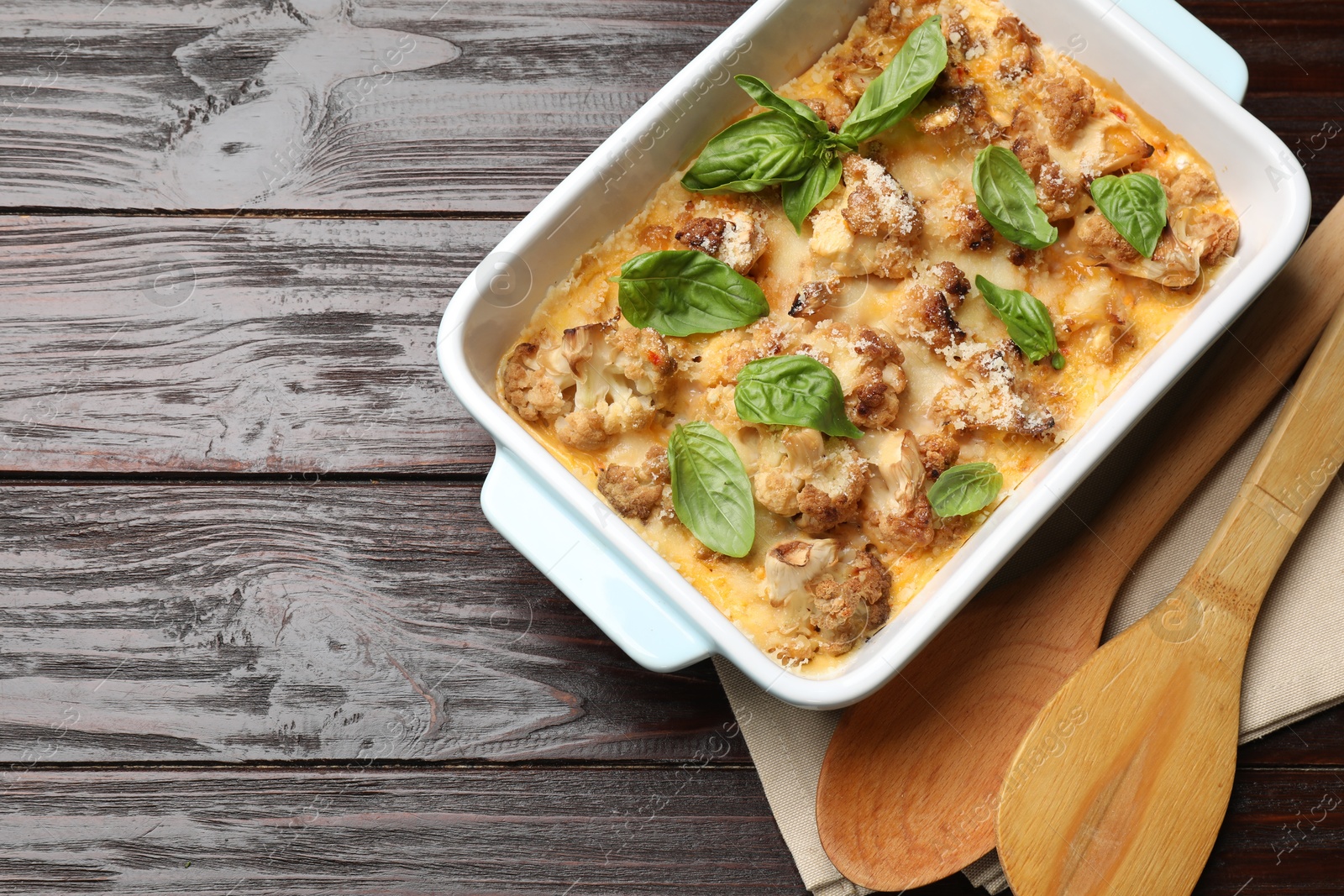 Photo of Tasty baked cauliflower and basil in baking dish on wooden table, top view. Space for text