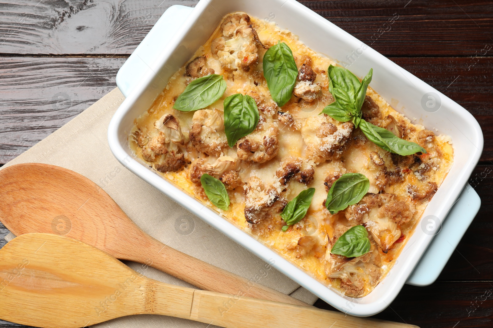 Photo of Tasty baked cauliflower and basil in baking dish on wooden table, top view