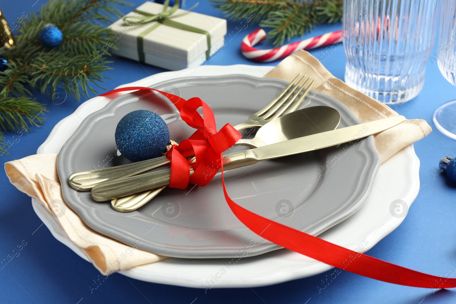 Photo of Beautiful Christmas setting with plates, elegant cutlery and festive decor on blue table, closeup