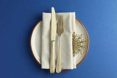 Photo of Beautiful Christmas setting with plate, elegant cutlery and golden snowflake on blue table, top view