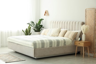 Photo of Large bed, houseplants and bedside table in stylish room