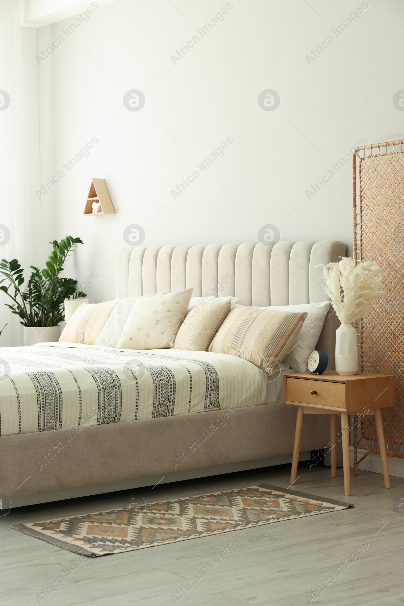 Photo of Large bed, houseplant and bedside table in stylish room