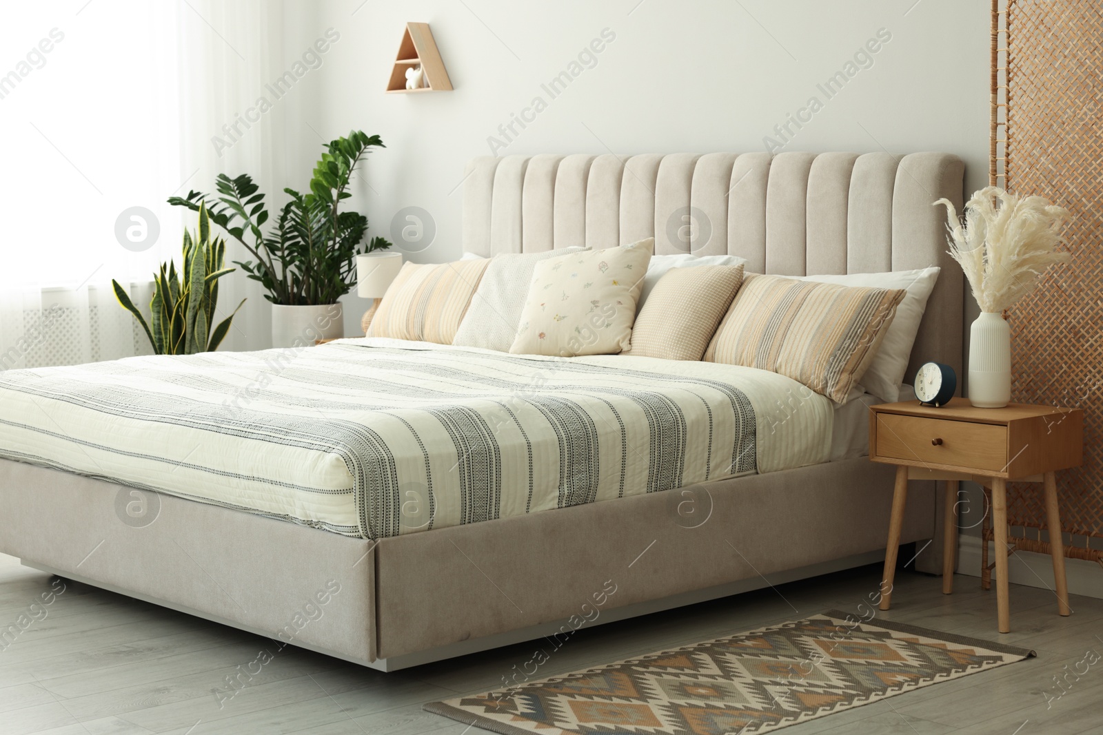 Photo of Large bed, houseplants and bedside table in stylish room