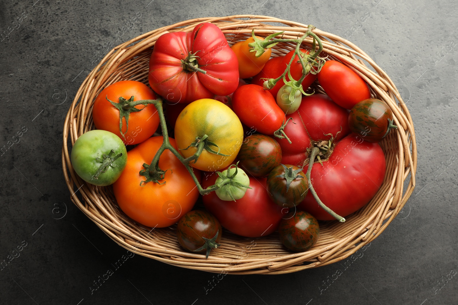 Photo of Different ripe and unripe tomatoes in wicker basket on grey table, top view