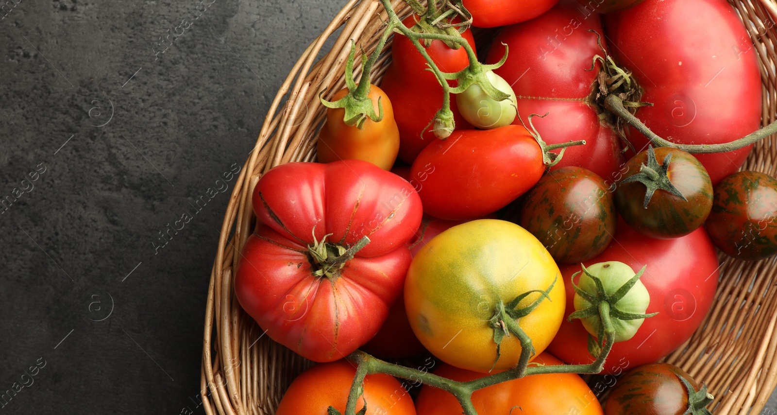 Photo of Different ripe and unripe tomatoes in wicker basket on grey table, top view