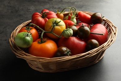 Different ripe and unripe tomatoes in wicker basket on grey table