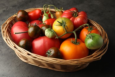 Photo of Different ripe and unripe tomatoes in wicker basket on grey table