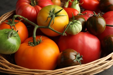 Photo of Different ripe and unripe tomatoes in wicker basket on table, closeup