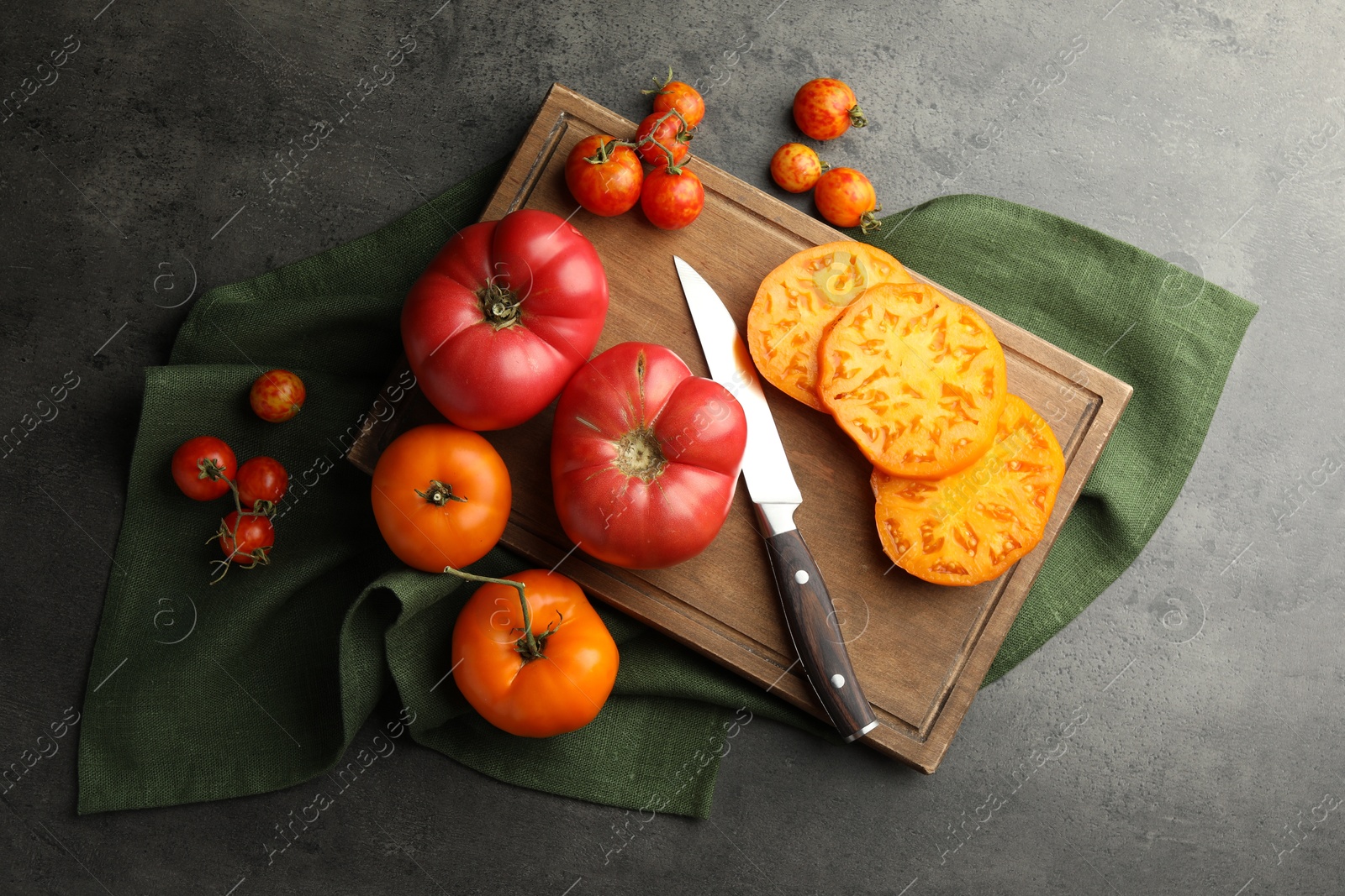 Photo of Whole and cut ripe tomatoes with knife on grey table, flat lay