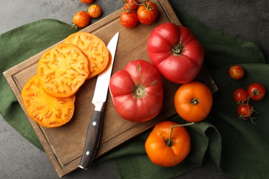 Photo of Whole and cut ripe tomatoes with knife on grey table, flat lay