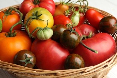 Different ripe and unripe tomatoes in wicker basket on white table, closeup