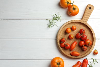 Different ripe tomatoes and rosemary on white wooden table, flat lay. Space for text